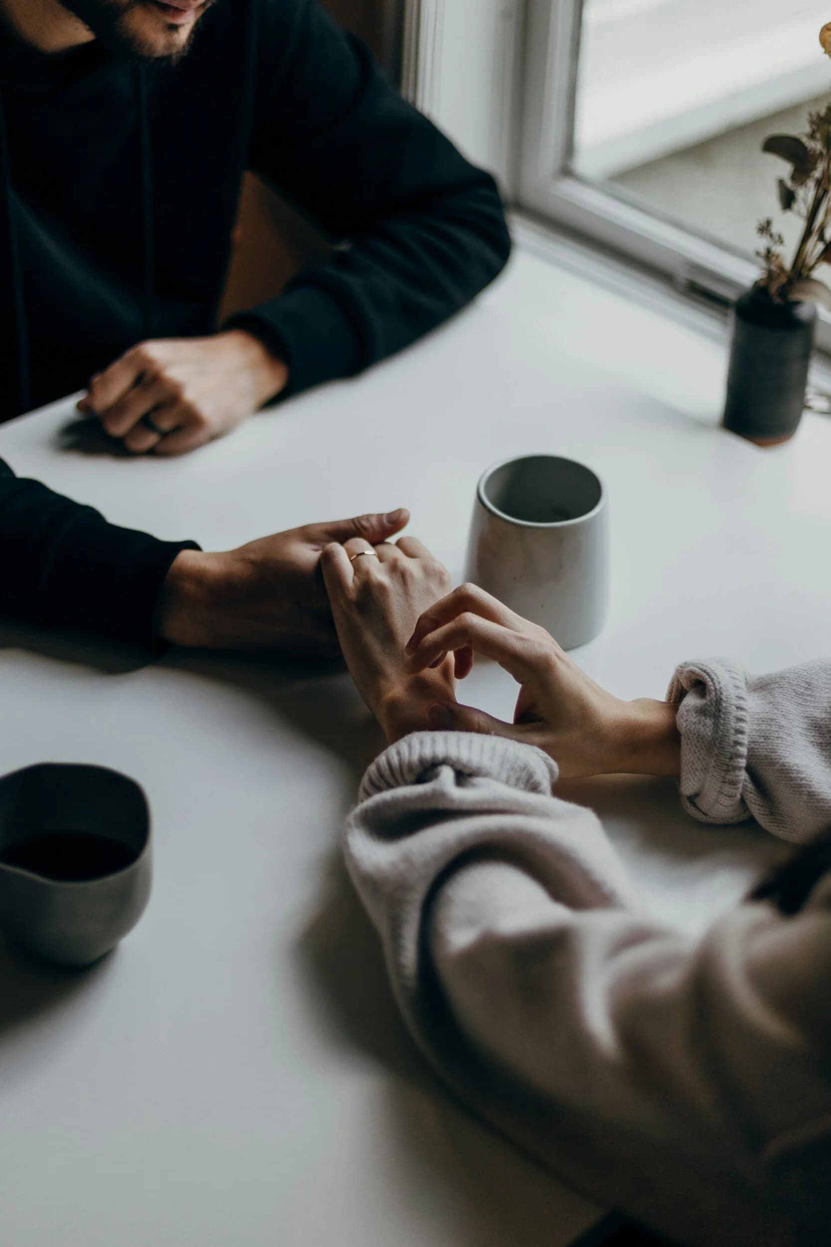two people holding hands across a table with coffee cups on the table