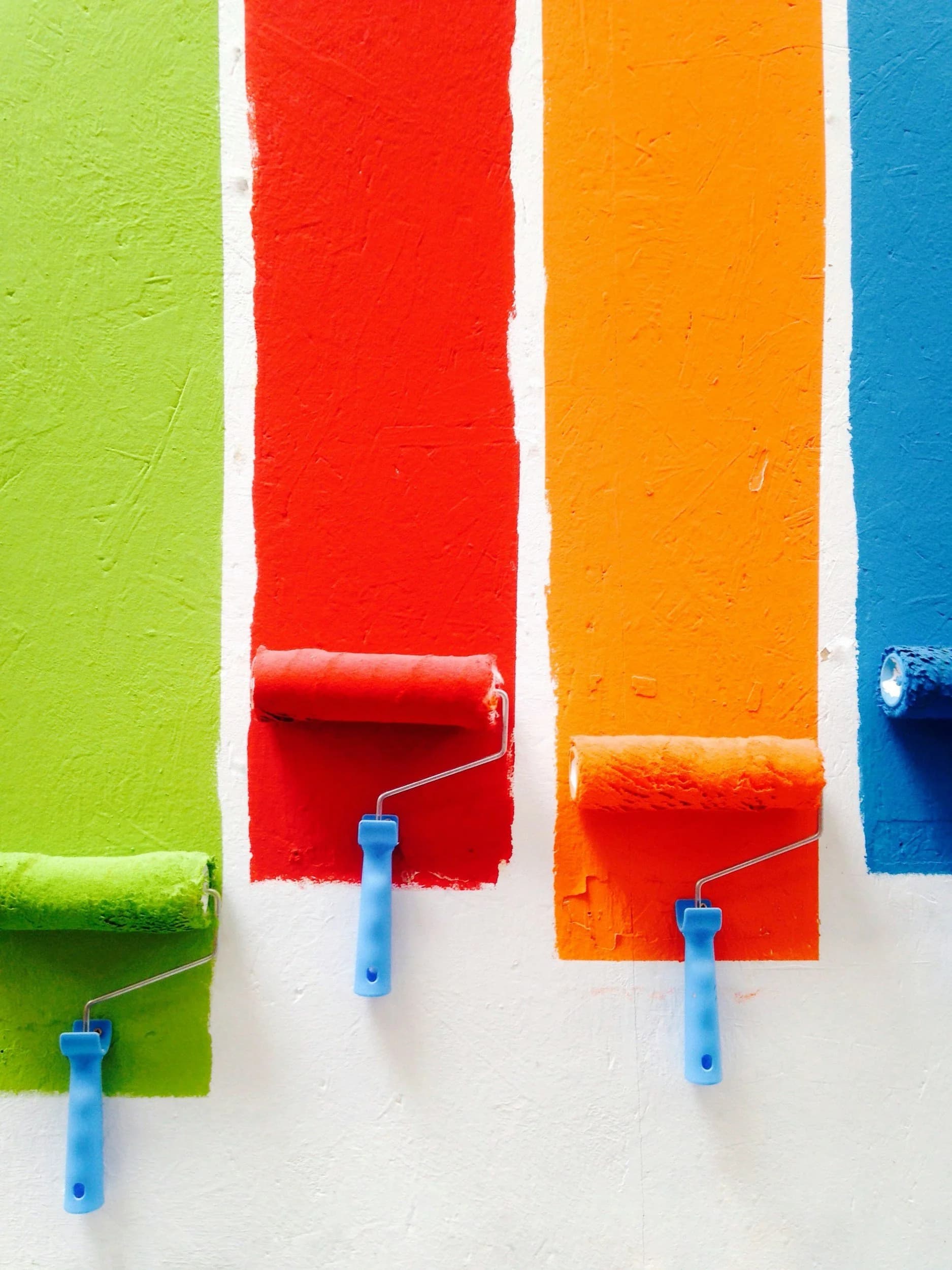 four coloured stripes of paint on a wall with paint rollers
