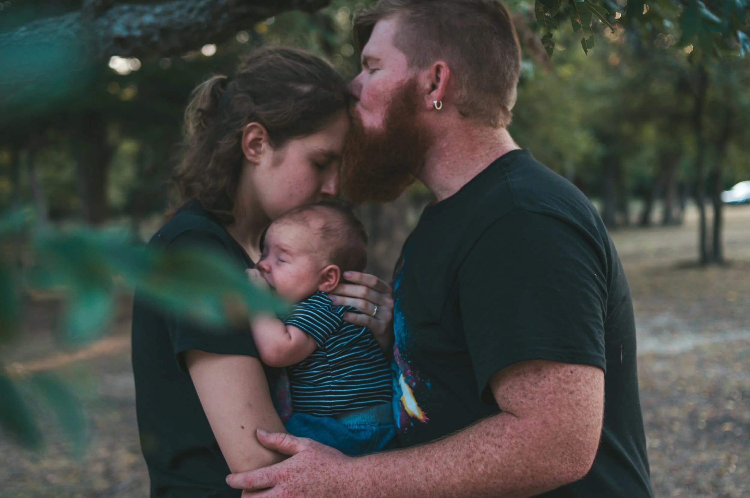 woman holding a baby with a man hugging her and kissing her forehead